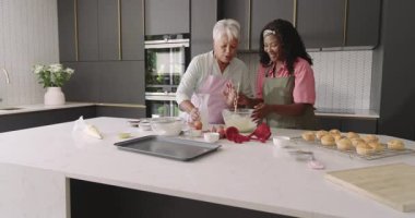 Üç nesil modern mutfakta birlikte yemek pişiriyor, kahkaha ve neşe paylaşıyor. Çeşitli aile, bağlılık, yemek pişirme, mutluluk, birliktelik, ev