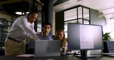 Çeşitli takımlar modern ofis ortamında dizüstü bilgisayardaki başarılı projeyi kutluyorlar. İşbirliği, takım çalışması, teknoloji, toplantı, iş, başarı