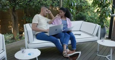Bahçede dinlenen, dizüstü bilgisayar kullanan ve veranda kanepesinde dokümanları inceleyen bir çift. Yaşam tarzı, uzaktan çalışma, eğlence, teknoloji, takım çalışması, iletişim