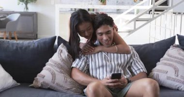 Açık planlı oturma odasında koyu gri kanepede akıllı telefonlarıyla sarılan sırıtan çift. Çağdaş, ev, tasarım, rahatlama, bağlantı, yaşam tarzı, iç mekan