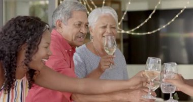 Şenlik ortamında çeşitli ailelerle şarap içen yaşlı bir kadın. Evde sıcak bir şekilde gülümsüyor. Kutlama, sevinç, sıcaklık