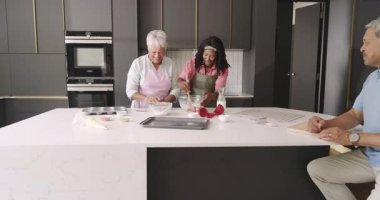 Üç nesil modern mutfakta birlikte yemek pişiriyor, kahkaha ve neşe paylaşıyor. Çeşitli aile, bağlanma, çok nesilli, mutluluk, yemek pişirme, birliktelik