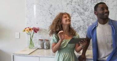 Stylus 'la birlikte ayakta duran çift mutfaktaki mermer tezgahta deniz kabuğu kavanozlarıyla tablet kullanıyor. Modern, lüks, minimalist, yaşam tarzı, ev, tasarım, teknoloji