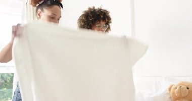 Yataktaki renkli kıyafetleri düzenlemek, farklı lezbiyen çiftler evde birlikte ev işleri yapmak. Çamaşır, temizlik, organizasyon, takım çalışması, ev hayatı, giysi