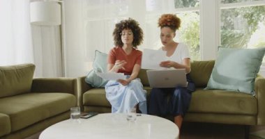 Aynı cinsiyetten lezbiyen çift evdeki parlak oturma odasındaki kanepede belgeleri gözden geçiriyorlar. LGBTQ, yaşam tarzı, ev, kağıt işleri, ilişki, yerli