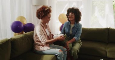 Eşcinsel çeşitlilikte lezbiyen bir çift evde doğum gününü kutluyor, hediyelerini değiş tokuş ediyor ve sıcak bir şekilde gülümsüyor. Kutlama, LGBT, mutluluk, aşk, hediyeler, birliktelik