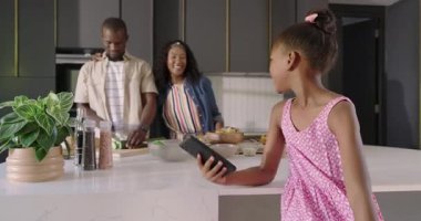 Ebeveynler modern mutfakta yemek hazırlarken genç bir kız selfie çekiyor. Çeşitli aile, yaşam tarzı, teknoloji, akıllı telefon, yemek pişirme, kaynaşma