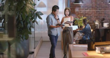 Asyalı erkek ve kadın modern ofiste gece tablet projesini tartışıyorlar. İş, teknoloji, takım çalışması, işbirliği, şirket, ofis hayatı