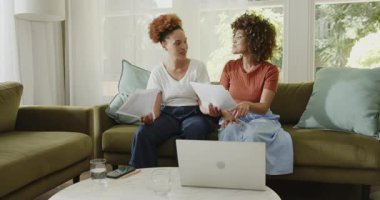 Çift cinsiyetli lezbiyen çift evdeki bilgisayarlı ve akıllı telefonlu belgeleri gözden geçiriyorlar. lgbtq, teknoloji, takım çalışması, iletişim, ilişki, ortaklık