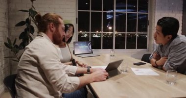 Geceleri iş birliği yapan, çeşitli profesyoneller ofiste dijital cihazlar kullanarak raporları tartışıyor. işbirliği, takım çalışması, teknoloji, iletişim, tartışma