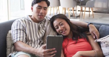 Gülümseyen çift modern oturma odasındaki gri koltukta kumaşlı minderlerle tablete bakıyor. Modern, gündelik, yaşam tarzı, iç mekan, arkadaşlık, teknoloji, konforlu