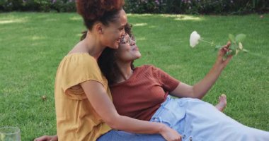 Aynı cinsiyetten farklı lezbiyen çiftler çimenlerde, güneşli bir günde ve bahçedeki beyaz gülde dinleniyorlar. lgbtq, romantizm, doğa, rahatlama, aşk, bağlantı