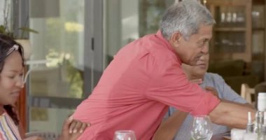 Çeşitli aileler evde birlikte yemek yerken yaşlı bir adam şarap dolduruyor. Toplanma, kutlama, yemek, birliktelik, yemek, kaynaşma