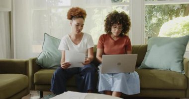 Evde, oturma odasındaki kanepede dizüstü bilgisayar kullanırken aynı cinsiyetten lezbiyen çift belgeleri tartışıyor. Çeşitlilik, ortaklık, lgbtq, iletişim, uzaktan çalışma, ev hayatı