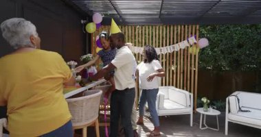 Baba, çeşitli ailelerin kutlamalarıyla birlikte dışarıda bir doğum günü partisinde kızını neşeyle kucaklıyor. kutlama, mutluluk, bağ, çocukluk, ebeveynlik