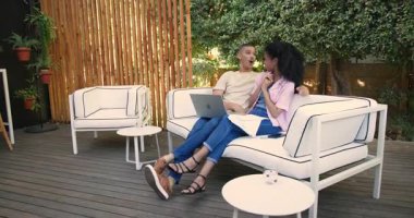Çeşitli çiftler avluda dizüstü bilgisayar kullanıyor ve bahçede birlikte atıştırmanın tadını çıkarıyorlar. Yaşam tarzı, eğlence, birliktelik, bağlanma, teknoloji, rahatlama.