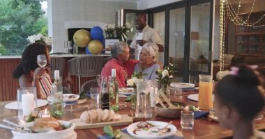 Evde doğum gününü kutluyoruz, farklı ailelerden insanlar akşam yemeğinde gülümsüyor. Kutlama, birliktelik, mutluluk, yemek, neşe, çoklu nesil