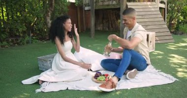 Çeşitli çiftler bahçede pikniğin tadını çıkarıyorlar. Güneşli bir günde şampanya ve taze meyve paylaşıyorlar. Romantik, kutlama, eğlence, yaz, birliktelik, yaşam tarzı