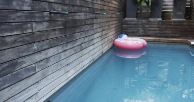 Bahçe havuzunda yüzen pembe şişme donut, plaj topu ve saksı bitkileriyle birlikte. Rahatlama, rahatlama, açık hava, minimalist, tropikal, yaz, dinginlik