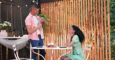 Kadın bahçe kafesinde heyecanla tepki verirken erkek şampanya şişesini açıyor. Kutlama, restoran, içecek, etkileşim, bahçede, şenlikli