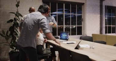 Çeşitli takımlar gece modern ofiste iş birliği yapıyor, dizüstü bilgisayarlı ekranda projeyi tartışıyorlar. İşbirliği, takım çalışması, beyin fırtınası, teknoloji, geç saatlere kadar çalışma, iş