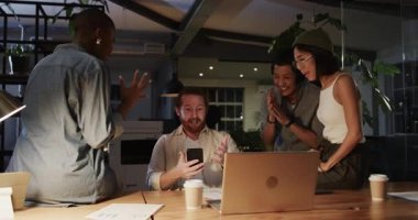 Ofis masasında başarıyı kutlayan çeşitli iş ekipleri dizüstü bilgisayar ve kahve fincanlarıyla. Takım çalışması, başarı, işbirliği, kutlama, toplantı, profesyonel