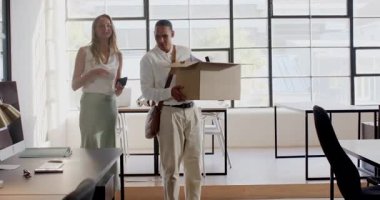 Muhtelif meslekdaşlar ofiste, adam çantalarını toplarken kadın akıllı telefonu tutuyor, gülümsüyor. İş arkadaşları, takım çalışması, iş dünyası, profesyonel, şirket, teknoloji