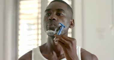 Afro-Amerikalı adam banyoda tıraş oluyor, mavi jilet ve tıraş köpüğüyle, fotokopi odası. Kişisel bakım, bakım, cilt bakımı, hijyen, minimalizm, kişisel rutin, sağlık