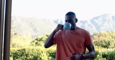 Afro-Amerikalı adam terasta dikilip mavi seramik bardaktan yudumluyor, fotokopi çekiyor. Rahatlama, rahatlama, açık hava, dinginlik, sağlık, yaşam tarzı, doğal