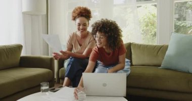 Evde rahat bir oturma odasında dizüstü bilgisayar kullanırken aynı cinsiyetten lezbiyen çift belgeleri tartışıyor. LGBTQ, takım çalışması, işbirliği, ilişki, teknoloji, ev