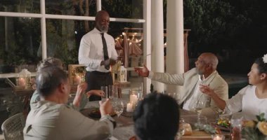 Düğünde, arka bahçedeki akşam yemeğinde zarif bir şekilde kadeh kaldırırken, misafirleri olan bir adam. Kutlama, çeşitlilik, toplanma, etkinlik, sofistike, çok kültürlü