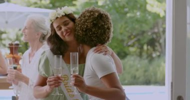 Çeşitli bayan arkadaşlar gelin adayını kutluyor, kollarını kavuşturuyor, verandada flüt kızartıyorlar. Kutlama, dostluk, zarafet, açık hava, eğlence, lüks, bağlantı