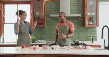 Mutfakta çeşitli çiftler birlikte yemek hazırlıyor, sebze doğruyor ve evde mutlu bir şekilde dans ediyorlar. Aşçılık, yaşam tarzı, ilişki, mutluluk, aşçılık, yerli