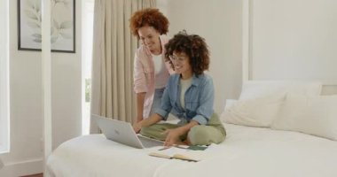 Çift cinsiyetli lezbiyen çift dizüstü bilgisayar kullanıyor ve evdeki yatakta notlar alıyor, mutlu bir şekilde iş birliği yapıyorlar. LGBT, işbirliği, teknoloji, yaşam tarzı, planlama, takım çalışması