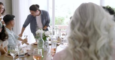 Arkadaşlarına el kol hareketi yapıp eğilmek, elbiseli bir kadın gül şarabı yetiştirmek ve masanın etrafında kahkahalar atmak. Kutlama, yoldaşlık, arkadaşlık, neşe, kahkaha, sosyalleşme, akşam yemeği.