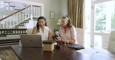 Evde kıdemli kadınlar yemek masasında birlikte gülüyor ve akıllı telefon kullanıyorlar. Yaşlılar, teknoloji, arkadaşlık, yaşam tarzı, iletişim, mutluluk