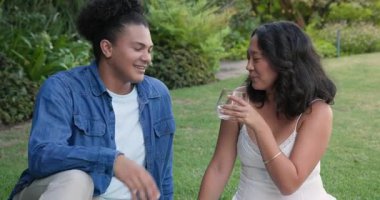 Bahçedeki çimenlerde oturmuş, içeceklerin tadını çıkarmak için sohbet eden, su kızartan ve üzüm toplayan bir çift. Romantizm, eğlence, dinginlik, piknik, zarafet, bağlantı, canlılık