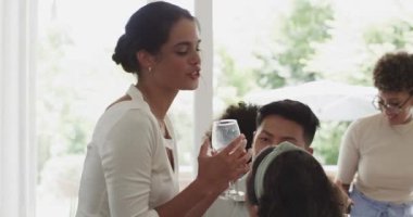 Çeşitli konuklar gülüyor ve şarap paylaşıyorlar. Masanın etrafında gül sunuyorlar, kopyalama alanı. Kutlama, neşe, zarafet, çeşitlilik, dostluk, sosyalleşme, yaşam tarzı..