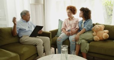 Çift cinsiyetli lezbiyen çift koltukta oturuyor, el ele tutuşuyorlar, evde desteklendiklerini hissediyorlar. lgbt, danışmanlık, terapi, akıl sağlığı, ilişki, iletişim