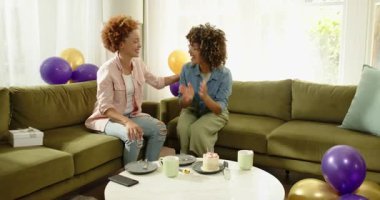 Evde doğum gününü kutluyoruz, neşeli lezbiyen çift kanepenin üzerinde kek ve kahvenin tadını çıkarıyor. Kutlama, mutluluk, ilişki, tatlı, içecek, yaşam tarzı