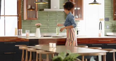 Çizgili önlüklü kadın modern mutfakta evinde çiçeklerle neşeyle dans ediyor. Aşçılık, yaşam tarzı, mutluluk, aşçılık, buket, neşe