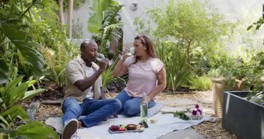 Bahçede piknik yapan, güneşli bir günde abur cubur ve içkileri paylaşan farklı çiftler. Açık hava, rahatlama, rahatlama, romantizm, doğa, birliktelik.