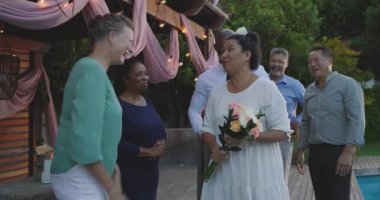 Bahçede evlilik yemini ederken, çeşitli çiftler ellerinde çiçekler, yakınlarda arkadaşlarıyla gülümsüyorlar. düğün, kutlama, mutluluk, arkadaşlık, evlilik, tören