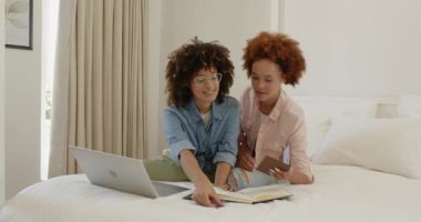 Aynı cinsiyetten lezbiyen çift yatakta dizüstü bilgisayar kullanarak oturuyor ve gülümsüyor, evde eğleniyor. lgbt, aşk, ilişki, teknoloji, bağlanma, birliktelik