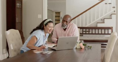 Evde dizüstü bilgisayar kullanan bir adam, yanında duran gülümseyen bir kadın. Teknoloji, takım çalışması, işbirliği, çeşitlilik, ortaklık, bağlantı