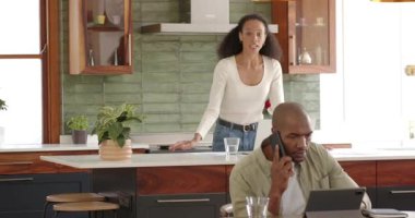 Kadın gazete okurken Afro-Amerikalı adam evde akıllı telefon ve tablet kullanıyor. Teknoloji, çoklu görev, iletişim, yaşam tarzı, boş zaman, kapalı alan