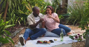 Çeşitli çiftler bahçede şarap ve aperatiflerle pikniğin tadını çıkarıyorlar. Rahatlama, yaz, açık hava