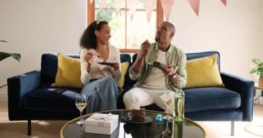 Çeşitli çiftler evde pasta ve şarabın tadını çıkarıyor, hediyeler ve gülümsemeyle kutluyorlar. Kutlama, romantizm, yıldönümü, yemek, hediye, misafirperverlik.