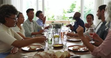 Çeşitli arkadaşlar yemek masasında kadeh tokuştururken Asyalı bir adam süs yerinde cam kaldırıyor. Kutlama, dostluk, neşe, sıcak atmosfer, sosyal toplanma, yaşam tarzı, kırsal kesim