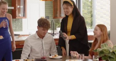 Çeşitli arkadaşlar mutfak adasında oturmuş tost için bardak kaldırırken sohbet ediyorlar. Sosyal toplanma, kutlama, keyiflilik, modern dekor, yoldaşlık, yaşam tarzı, şenlik